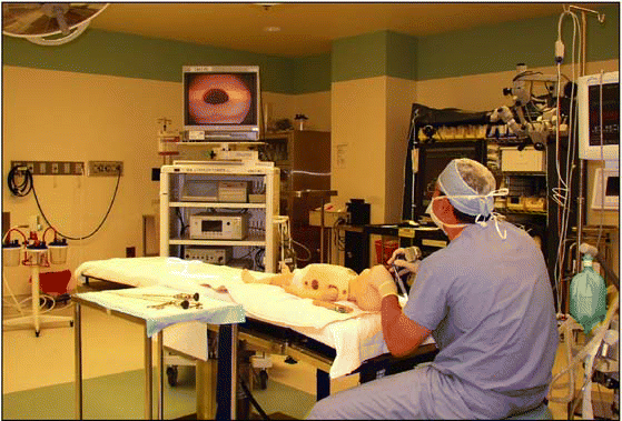 Figure. An otolarygology resident at Alfred I. Dupont Children's Hospital is using a scope to perform direct laryngoscopy and bronchoscopy to assess whether a foreign body in present in the mannequin's airway. He is watching the image of the infant's subglottis on a monitor.